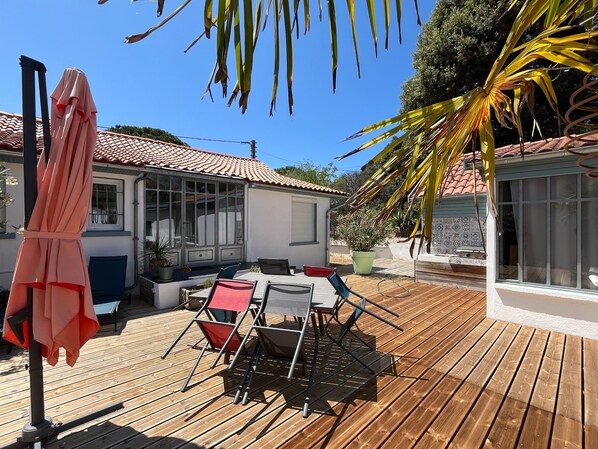 Una terraza de madera con mobiliario exterior, una mesa cubierta y una planta en maceta.