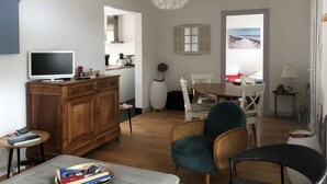 Un salon équipé d’un téléviseur, d’un meuble en bois, de fauteuils en osier, d’une table à manger et offrant une vue à travers une porte.