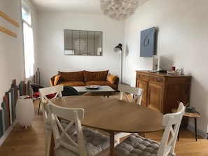 Una sala de estar moderna con una mesa de comedor de madera, sillas blancas, un sofá marrón y un mueble de madera.
