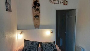 Un dormitorio con cama, dos almohadas, un adorno de tabla de surf en la pared, un accesorio de luz en el techo y una puerta.