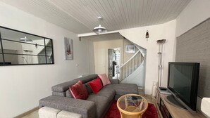 Una sala de estar con un sofá gris, cojines rojos, una mesa de centro de vidrio, un televisor y una escalera que sube a otro nivel.