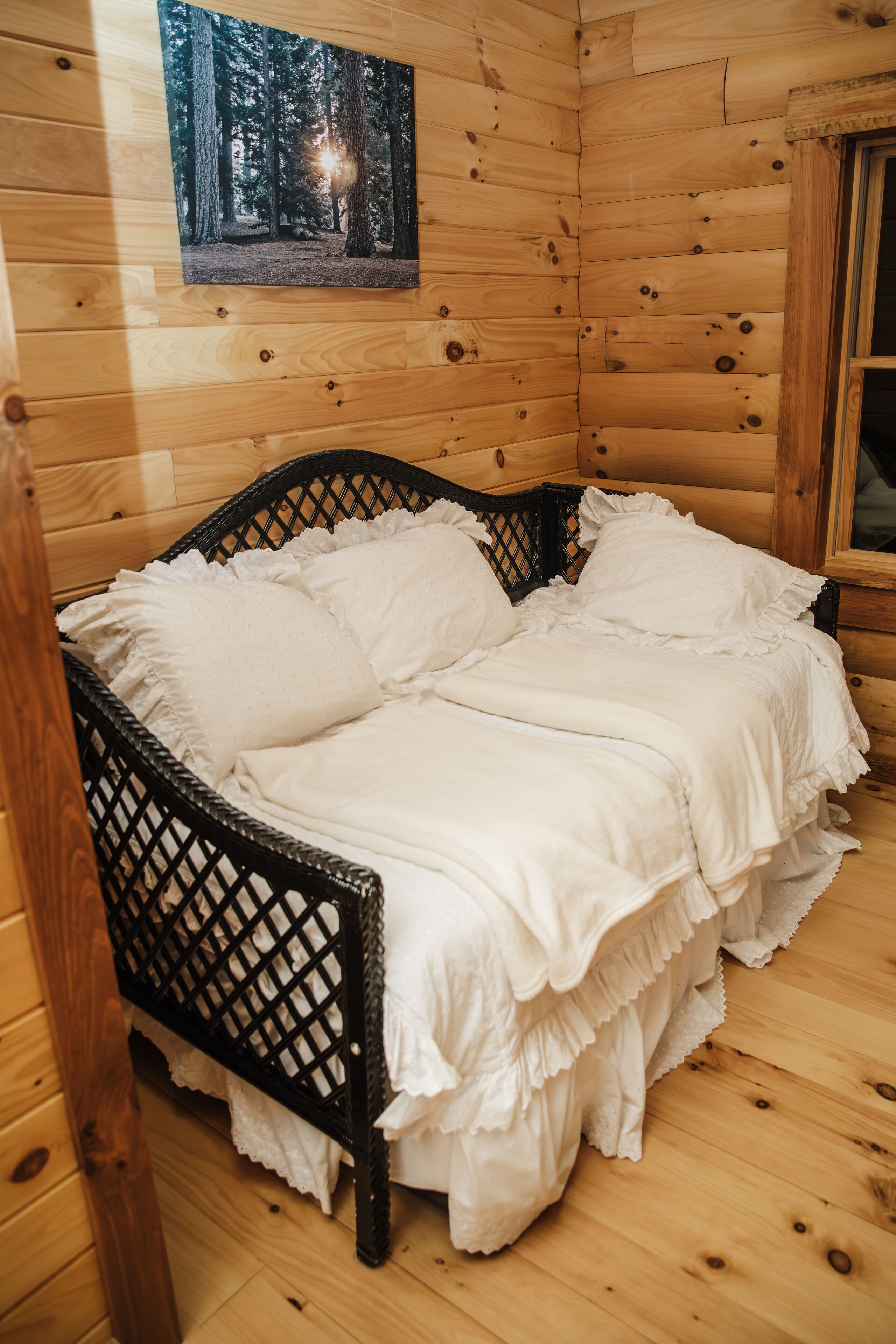 A wooden cabin room with a bed, a framed photo on the wall, and a window.