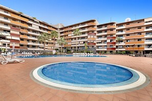A hotel with a swimming pool, multiple balconies, and a clear blue sky.