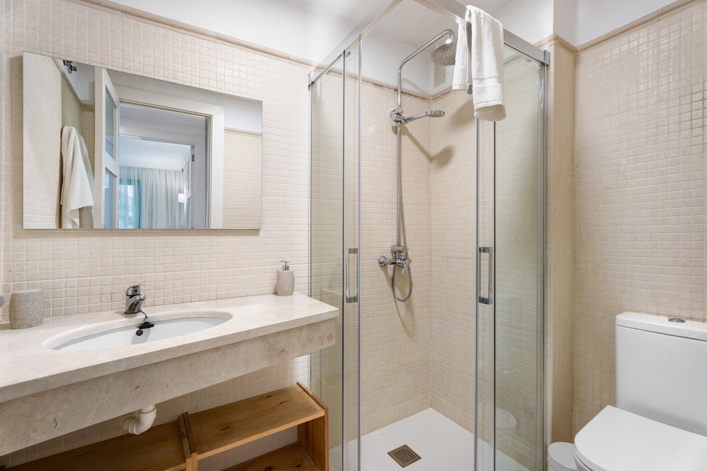 A bathroom with a glass-enclosed shower, a sink with a mirror above it, and a toilet.