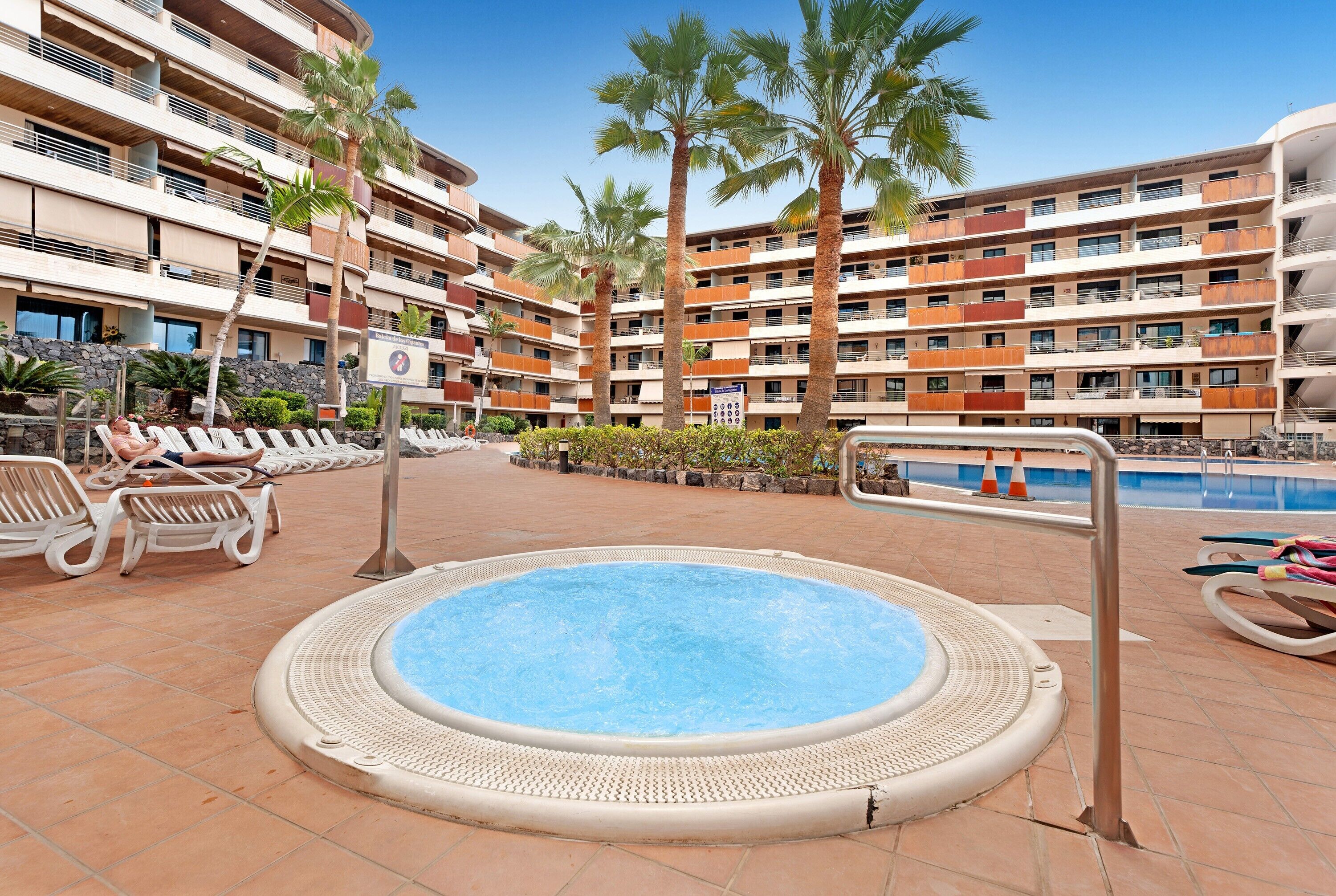 A hotel pool area with lounge chairs, a hot tub, and palm trees.