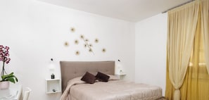 A modern bedroom with a large bed, two bedside tables, a wall-mounted lamp, and a potted plant. - LIBERA HOUSE Sweet apartments (San Salvo)