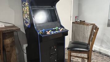 Una máquina de videojuegos retro con la etiqueta "Arcade Classics", un joystick y botones, una silla de madera y un suelo con estampado de piedra.