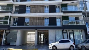 A multi-story residential building with balconies, a garage entrance, and a car parked in front.
