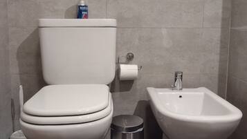 Un baño con inodoro, bidé y cubo de basura.