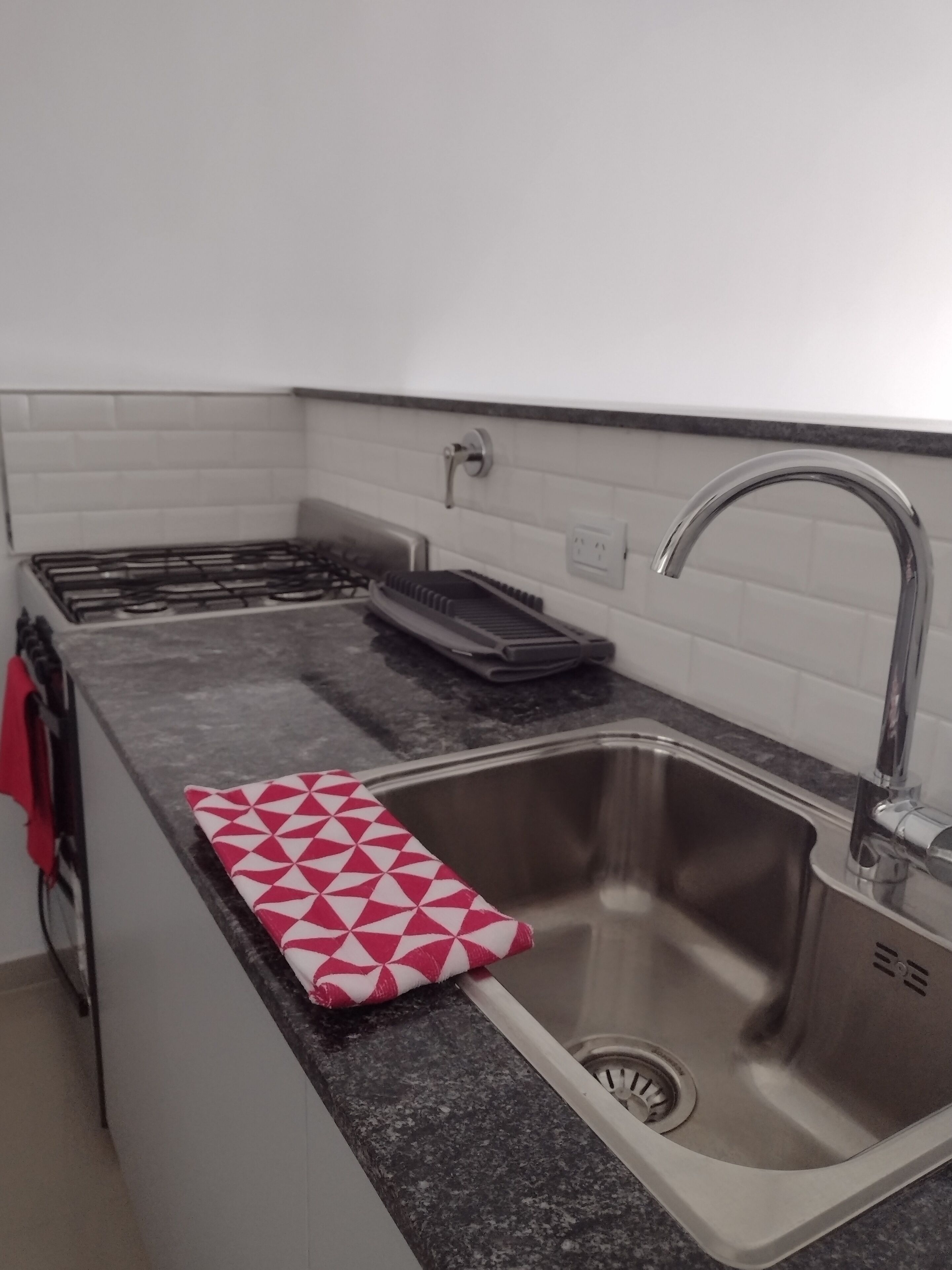 Una cocina con un lavamanos de acero inoxidable, una estufa a gas y una toalla roja y blanca con diseño en la encimera.