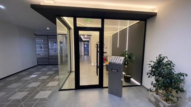 A modern hotel lobby with a glass door entrance, a reception desk, and a potted plant.