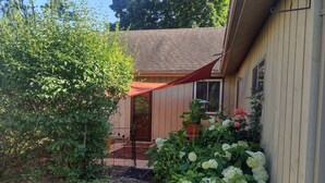 A wooden house with a covered porch, a gravel pathway, and lush greenery including hydrangeas and a large tree. - TRAVELERS! In the heart of Baraboo, close to SSM Hospital! (Baraboo)