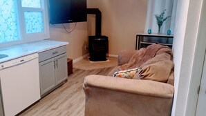 A compact living space with a kitchenette, a sofa, a flat-screen TV, and a wood-burning stove. - TRAVELERS! In the heart of Baraboo, close to SSM Hospital! (Baraboo)