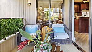 A balcony with wicker furniture, a glass table, and potted plants.