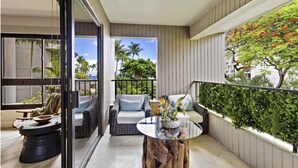 A balcony with wicker furniture, a glass table, and a view of palm trees and a building.