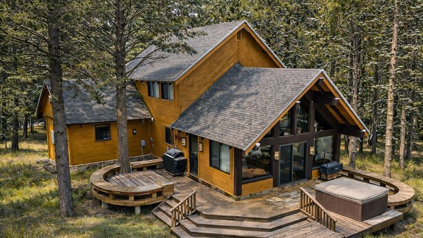 Eine Hütte mit einer großen Terrasse, Sitzgelegenheiten im Freien und einem Kamin.