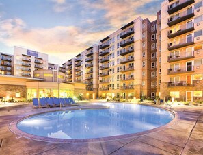 A hotel with a swimming pool surrounded by multiple-story buildings, outdoor seating, and a well-lit environment. - Seaside!! Condo with ocean view, grill on balcony, beach access from the resort. (Seaside)