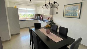 A modern kitchen with white cabinets, a black countertop, and a dining area with a black table and chairs. - Holiday apartment with balcony (Kampor)