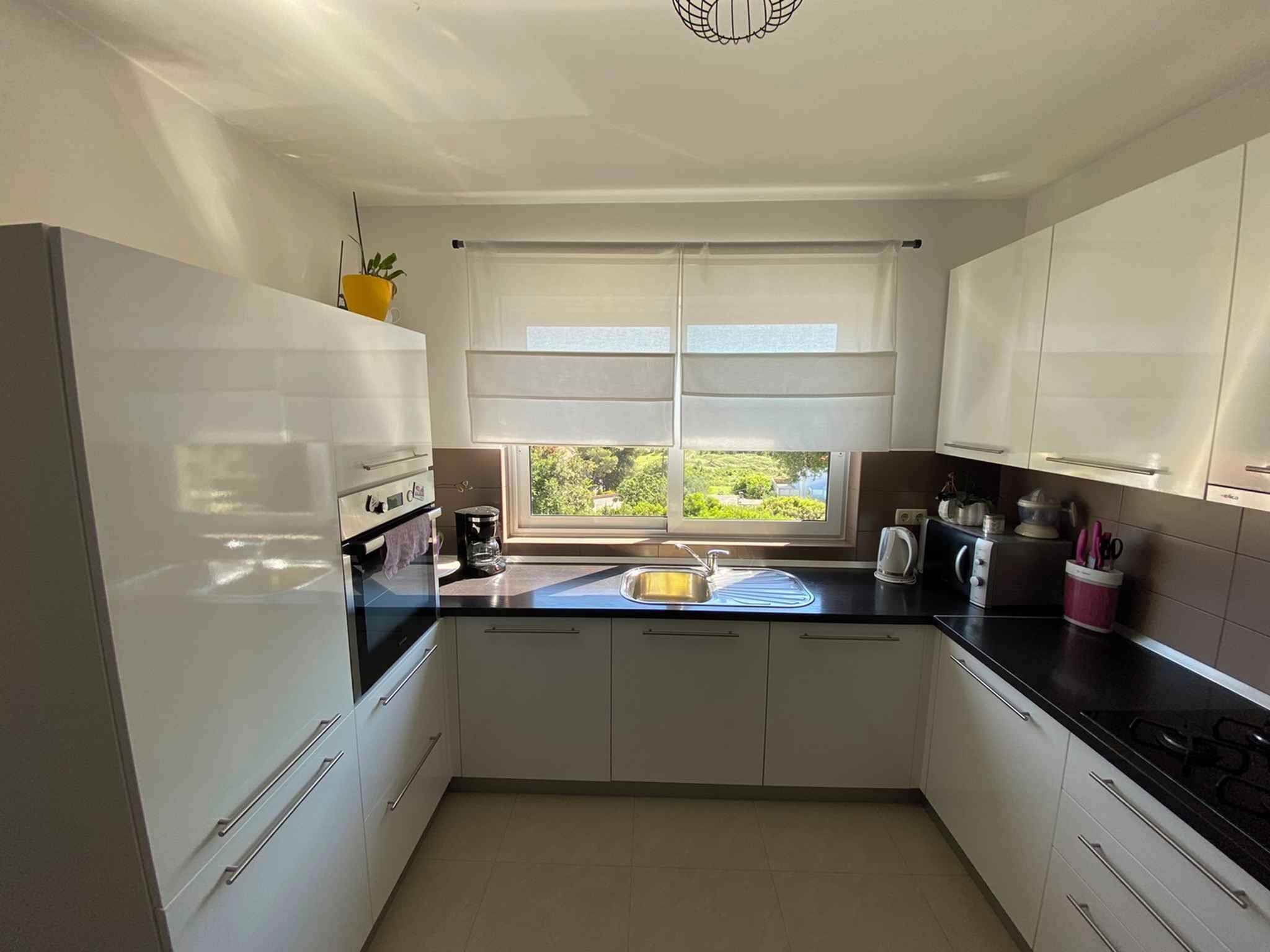 A modern kitchen with white cabinets, a black countertop, and a window providing a view of greenery outside.