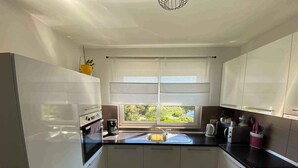 A modern kitchen with white cabinets, a black countertop, and a window providing a view of greenery outside. - Holiday apartment with balcony (Kampor)