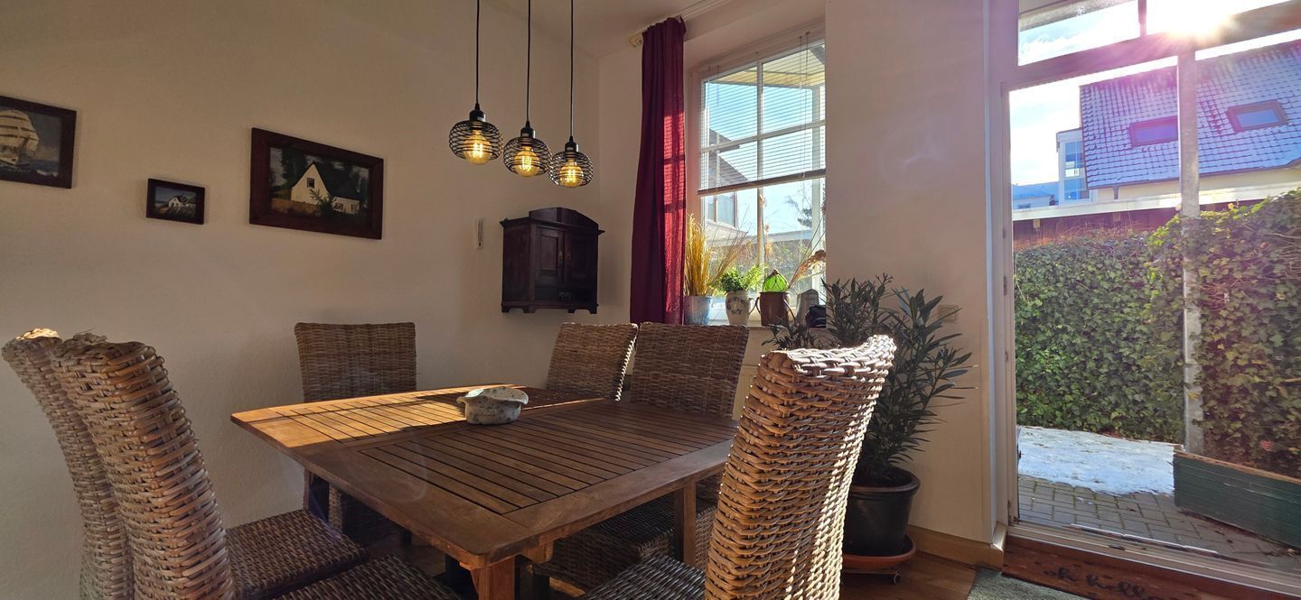 Un coin repas avec une table en bois et des chaises en osier, un buffet et des lampes suspendues.