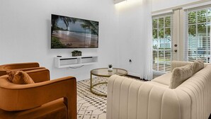 Un salon moderne avec un grand téléviseur à écran plat, un canapé beige, un fauteuil marron et une table basse en verre.