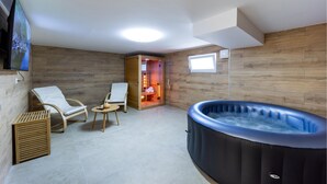 Une salle de spa équipée d’un bain à remous, de deux fauteuils, d’une petite table et d’un mur en bois.