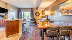 Una habitación de hotel moderna con área de cocina, una mesa de comedor con sillas, un sofá y un gran ventanal con vistas.