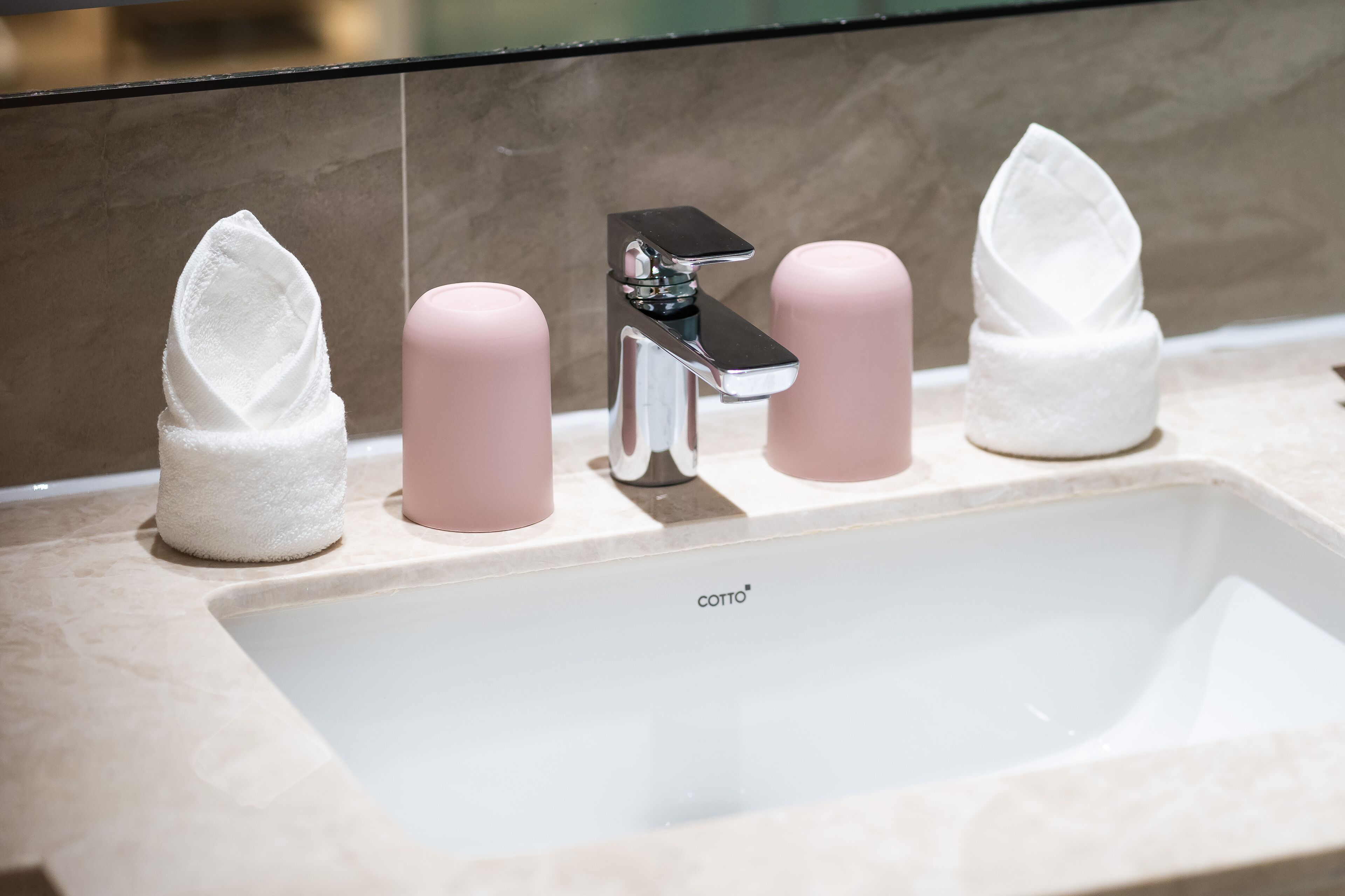 A bathroom sink with a COTTO brand faucet, two pink soap dispensers, and two white napkin holders.
