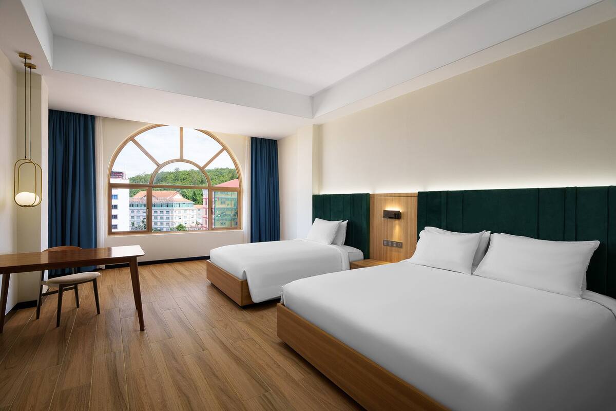 A hotel room with two beds, a desk, and a large window with curtains.
