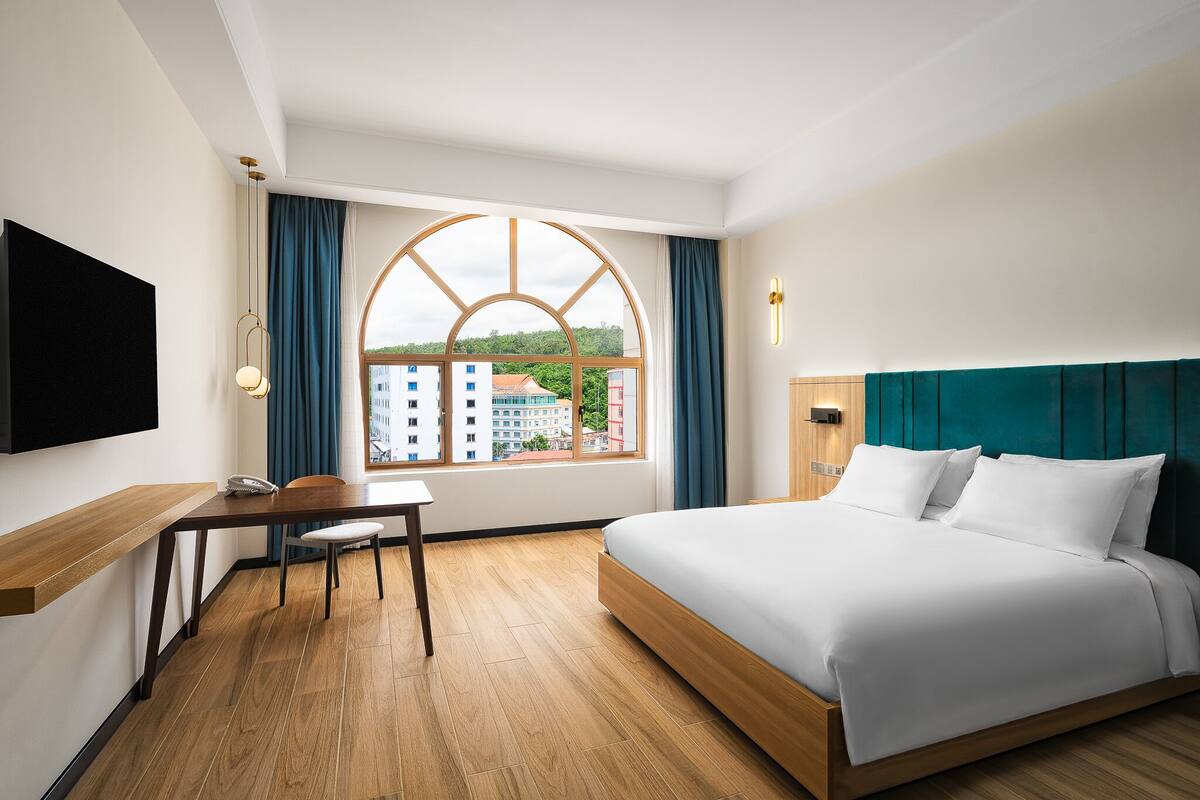 A hotel room with a large bed, a desk, and a TV.
