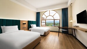 A hotel room with two beds, a wooden desk, a TV, and a large window with a view of the countryside. - Grand Pailin Casino & Resort (Sala Krau)