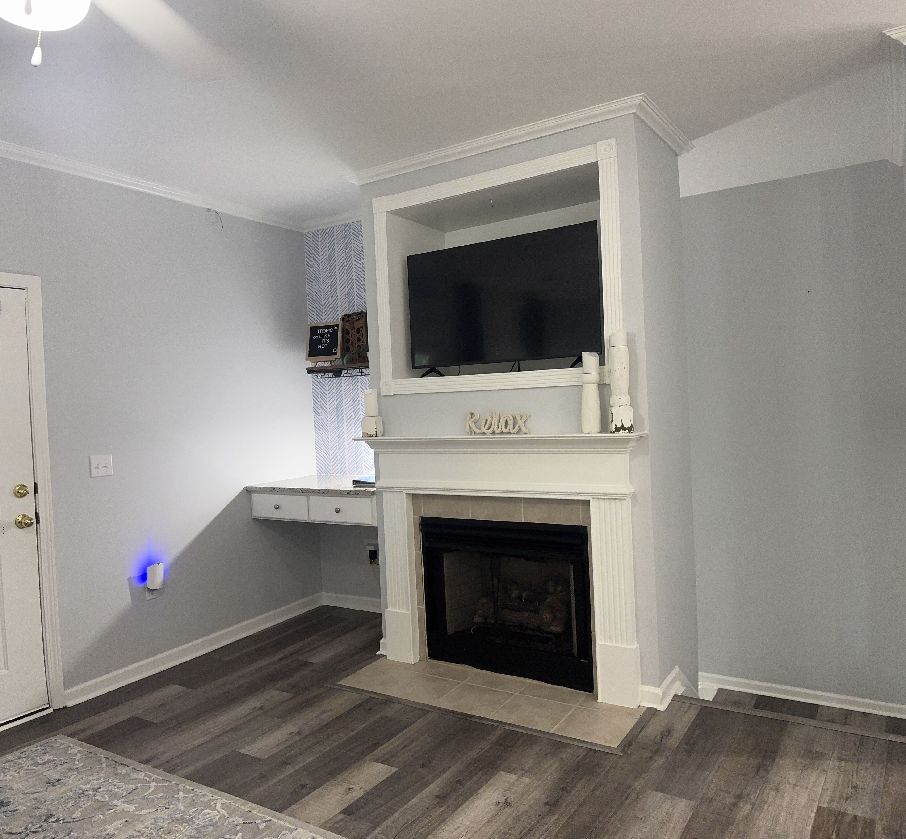 A room with a fireplace, a mounted TV, and a small shelf with decorative items.