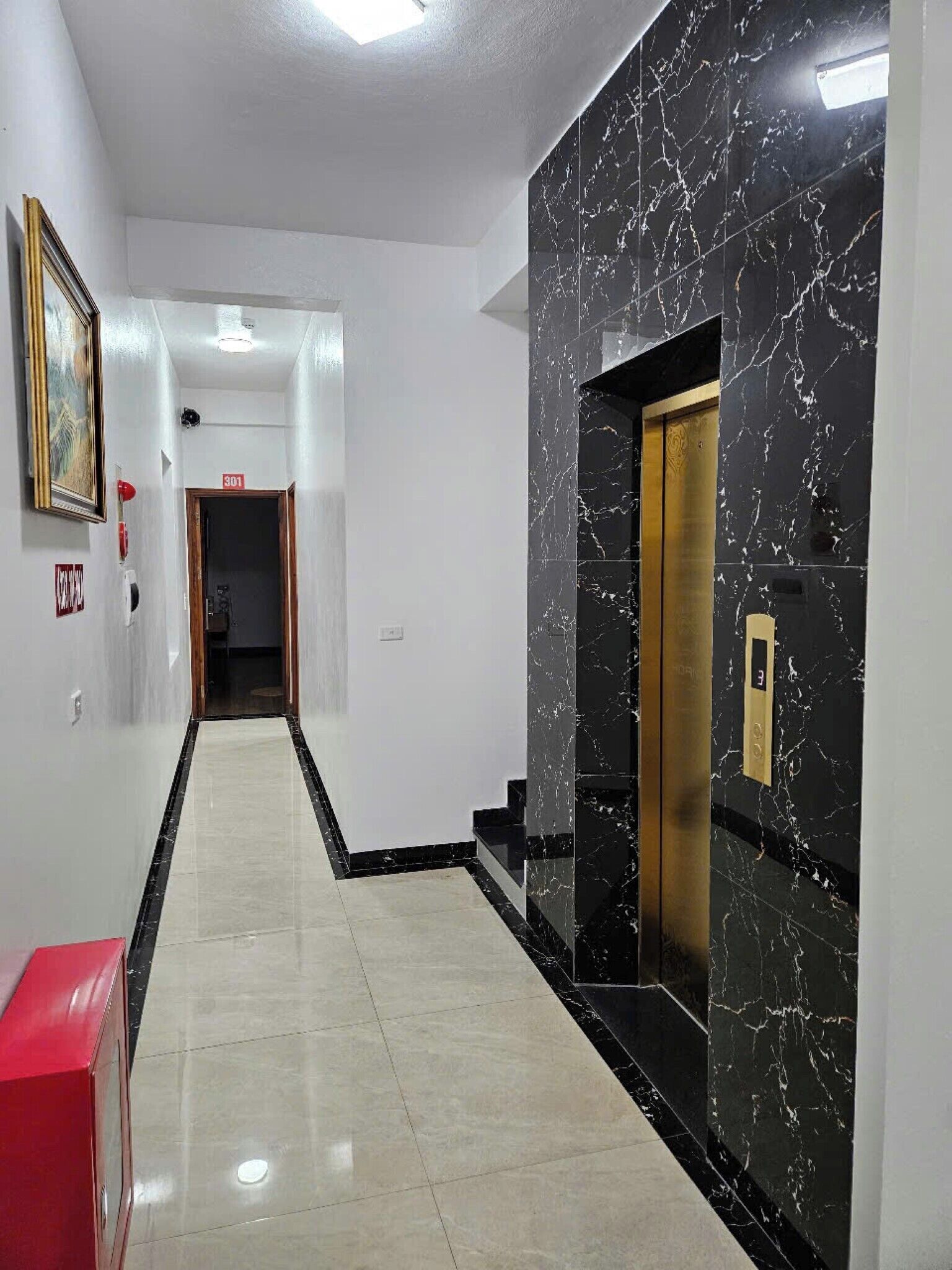 A hallway with a marble wall, a red bench, and an elevator.