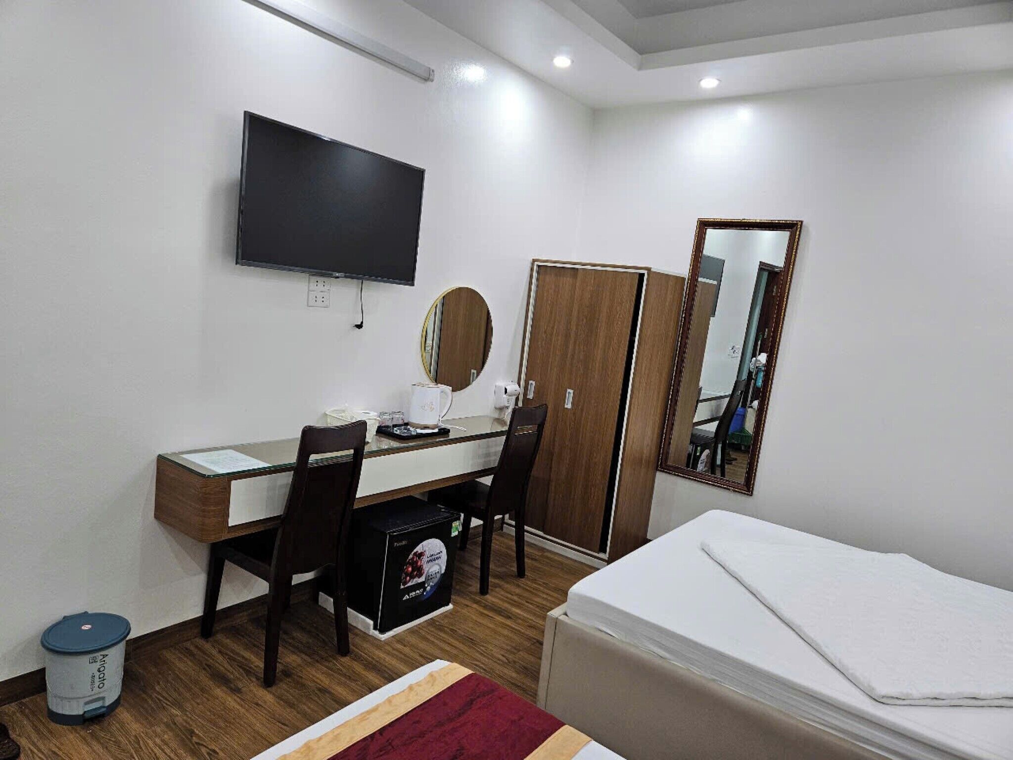A hotel room with a bed, a desk with a chair, a television, a wardrobe, and a mirror.