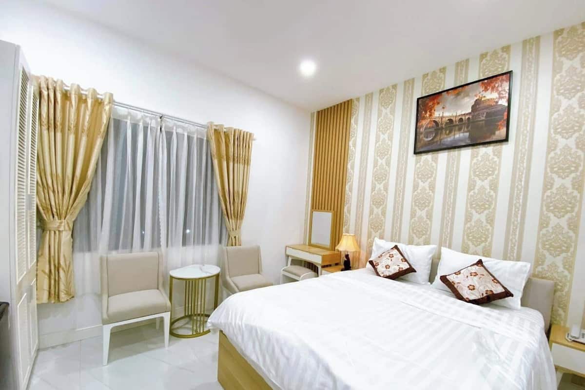 Une chambre d’hôtel avec un lit, deux chaises, une petite table ronde, une table de chevet avec une lampe et un tableau au mur.