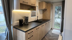 A modern kitchen with wooden cabinets, a black countertop, a coffee maker, and a window with curtains. - Tiny Haus Antonia by Interhome (Riedenburg)