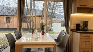 A modern kitchen with wooden cabinets and a dining area with a glass table and chairs. - Tiny Haus Antonia by Interhome (Riedenburg)