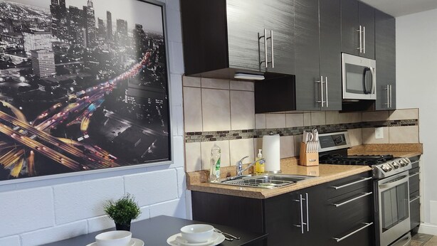 Una cucina moderna con mobili scuri, un forno a microonde, fornelli e un'area pranzo con tavolo e sedie.