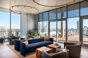 Um lounge moderno com um sofá azul, poltronas de couro e uma grande janela com vista para a cidade.