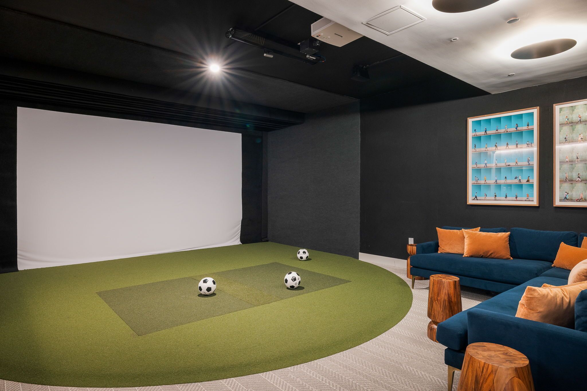 A home theater room with a large screen, a blue sofa, and a green carpet with soccer balls.