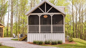 A lodge with a covered deck, outdoor seating, and a view of the surrounding forest.