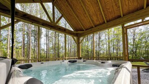 A hot tub with a wooden deck and a forest view.