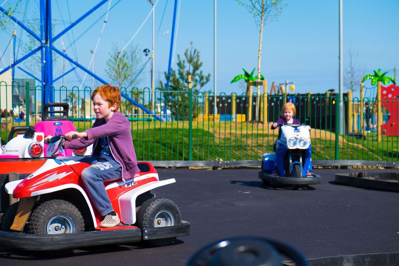 Ein Kind fährt mit einem kleinen, roten und weißen Spielzeugfahrzeug in einem Freizeitbereich im Freien.