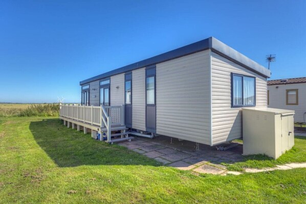Une maison mobile de plain-pied, dotée d’un toit plat, d’une véranda et d’un petit abri de jardin attenant.