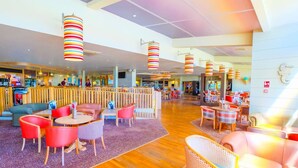 Un hall d’entrée spacieux doté d’un plancher en bois, de lampes suspendues à rayures rouges et blanches, et de différents types de mobilier, notamment des canapés et des tables.