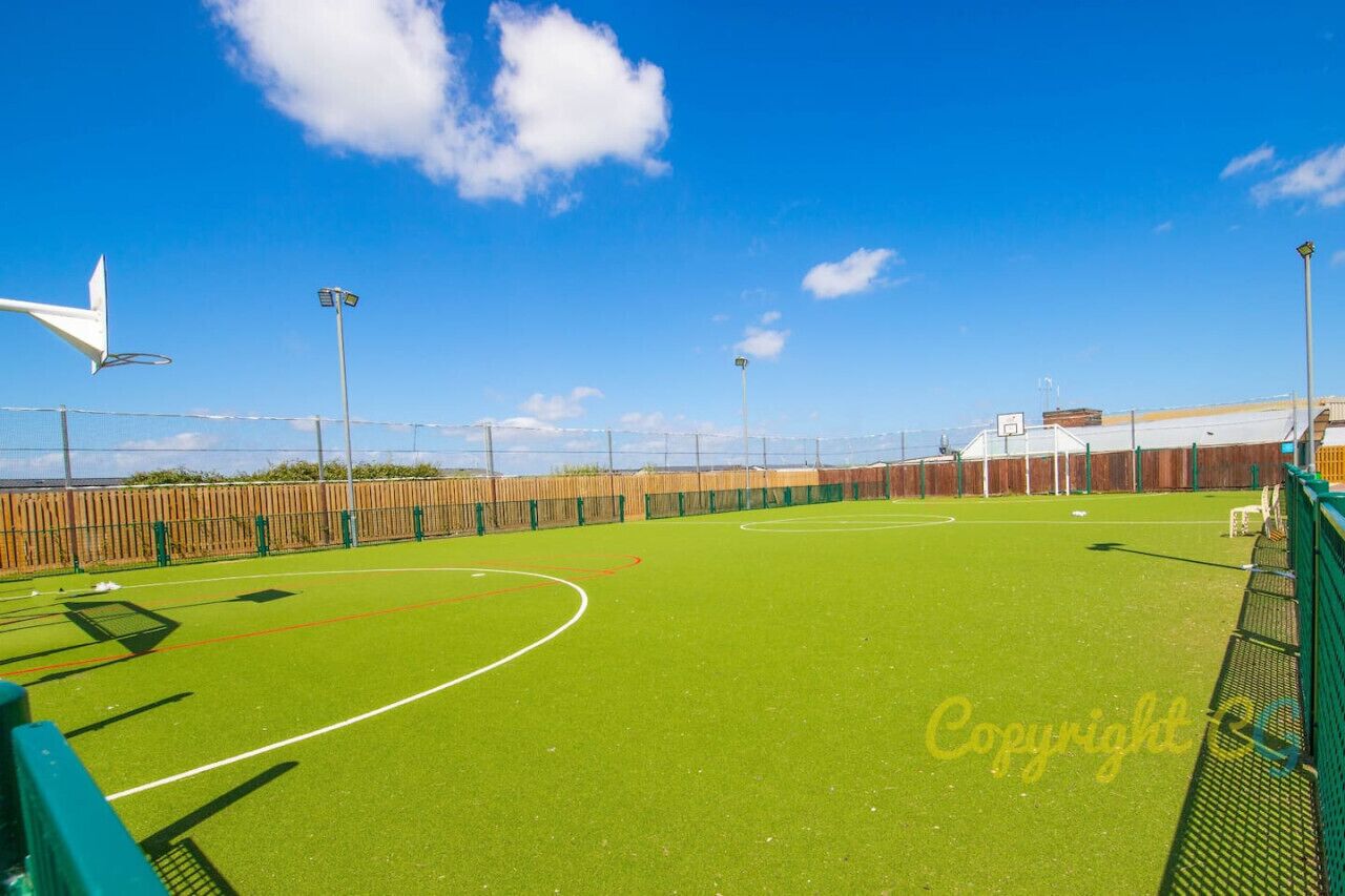 An outdoor sports field with a fenced boundary, goalposts, and floodlights.