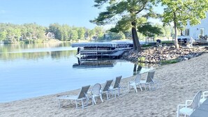 A lakeside beach with white lounge chairs and a dock with boats. - Dells Lake Villa - Lake Front Luxury (Wisconsin Dells)