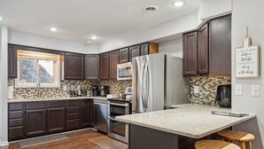 A modern kitchen with dark wood cabinets, stainless steel appliances, a large island with stools, and a decorative sign on the wall. - Dells Lake Villa - Lake Front Luxury (Wisconsin Dells)