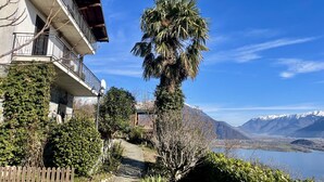 Un bâtiment doté d’un balcon, entouré de verdure et offrant une vue sur des montagnes et un lac.